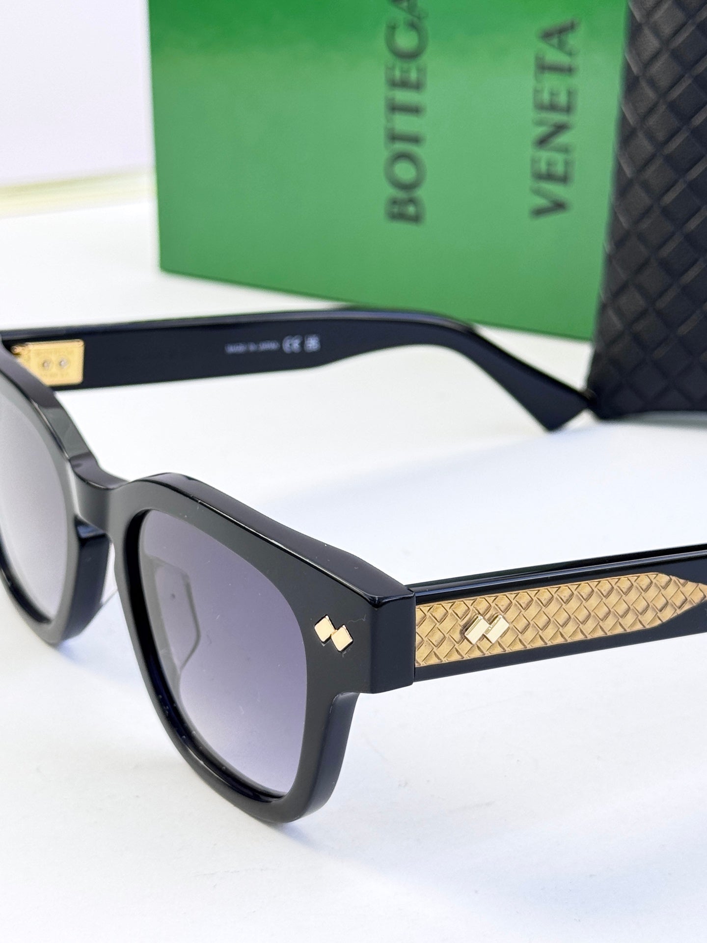 Black sunglasses close-up with textured gold temple band and tinted lenses