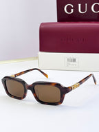 Tortoiseshell Gucci sunglasses with square frames, amber lenses, and gold-toned arm ornament.