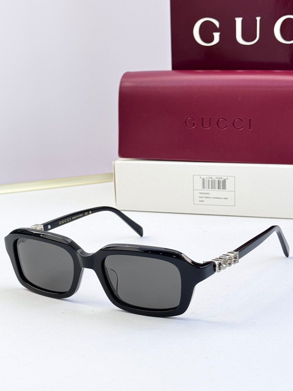 Black Gucci sunglasses with rounded-square frames, dark lenses, and silver-toned chain ornament.