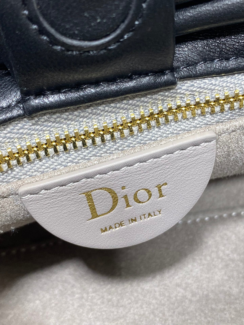 White Dior logo patch on black leather bag near gold zipper
