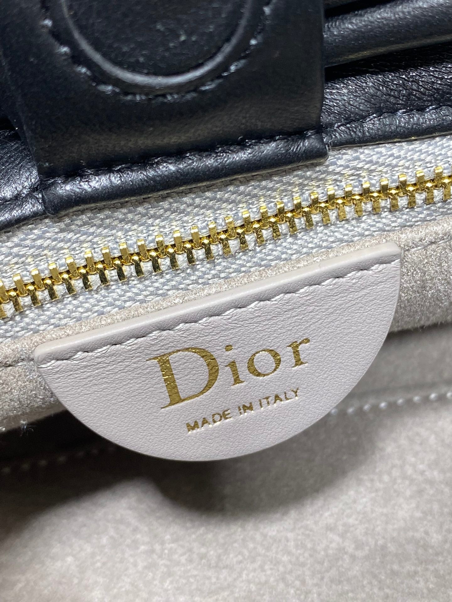 White Dior logo patch on black leather bag near gold zipper