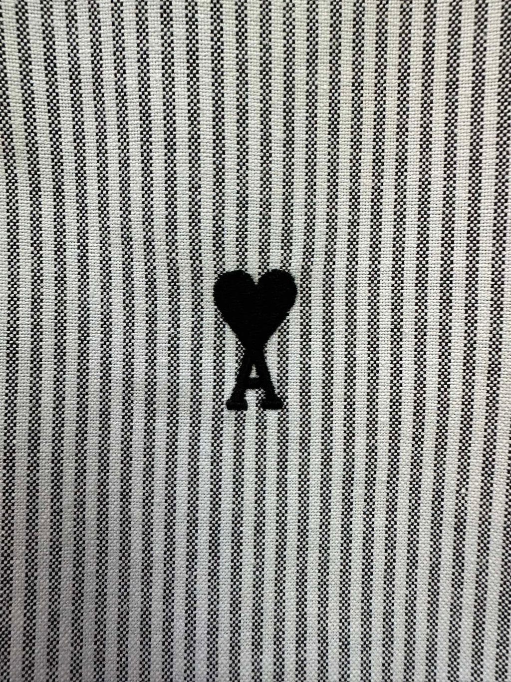Striped shirt fabric detail with small black heart-shaped A logo on chest