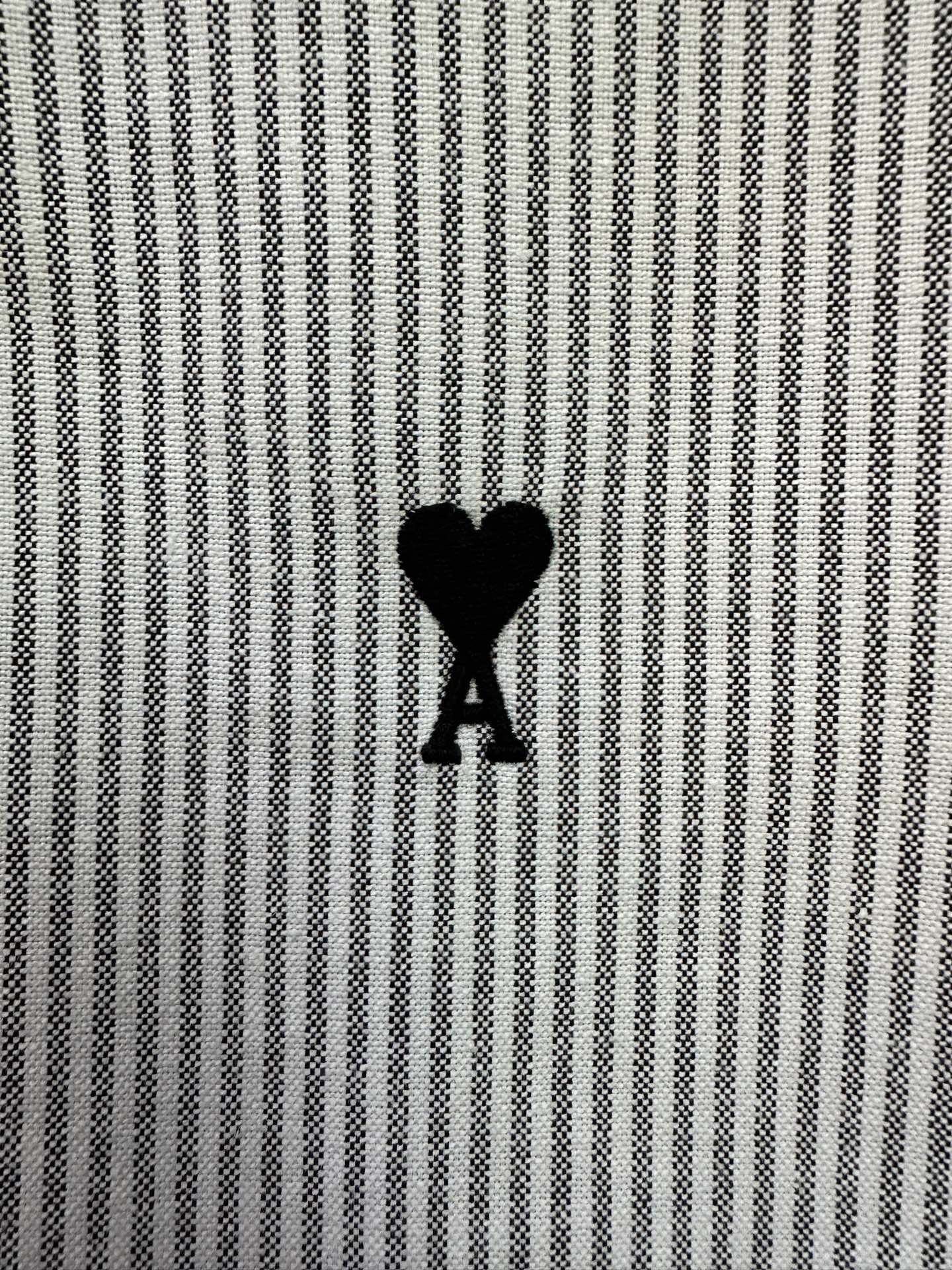 Striped shirt fabric detail with small black heart-shaped A logo on chest