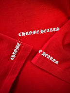 Red T-shirt with embroidered “Chrome Hearts” logos on sleeve and cuff.