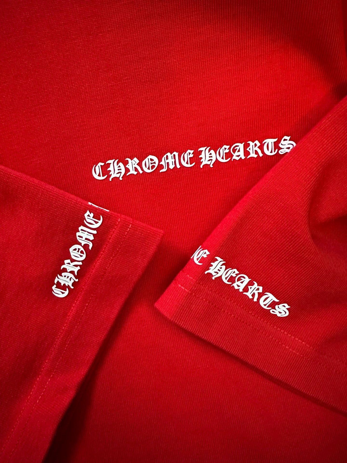 Red T-shirt with embroidered “Chrome Hearts” logos on sleeve and cuff.