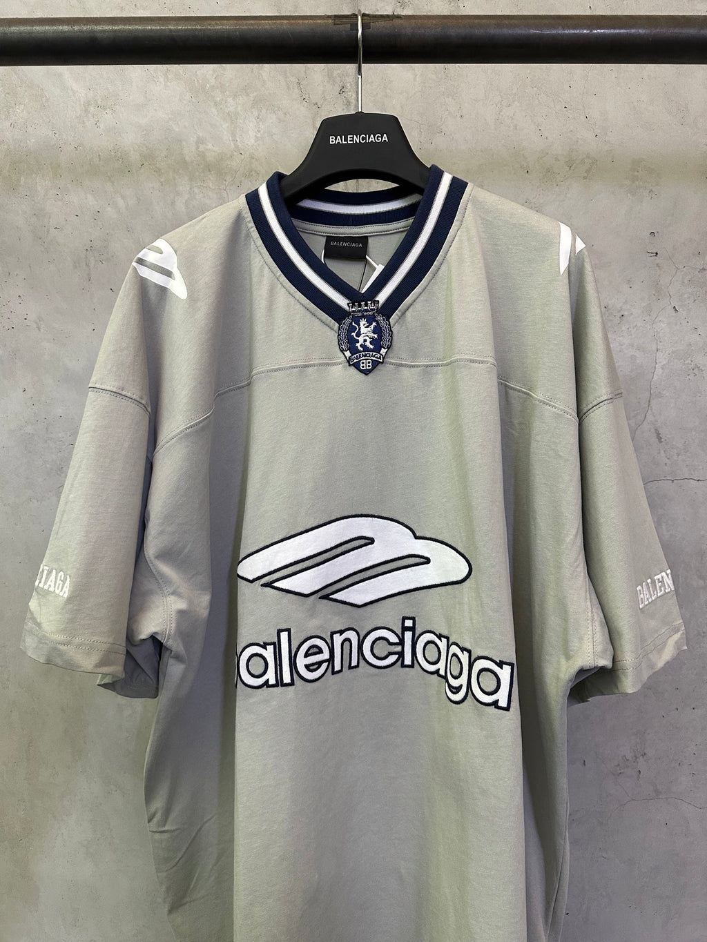 Light sage short-sleeve T-shirt with navy striped V-neck collar and crest patch