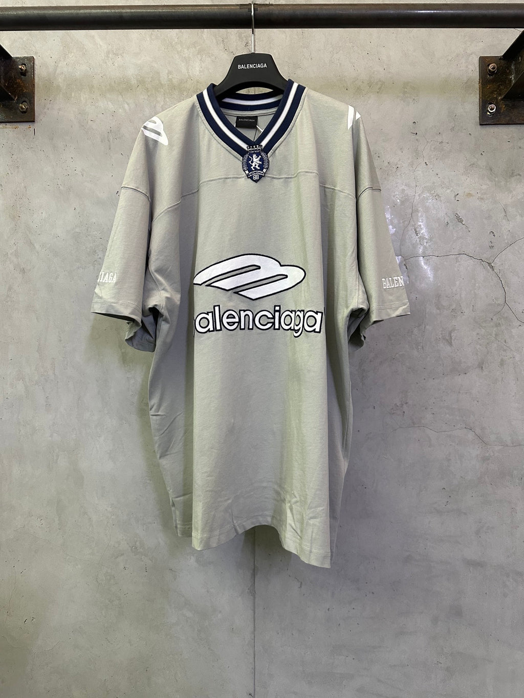 Light sage short-sleeve T-shirt with navy striped collar and crest patch at neckline