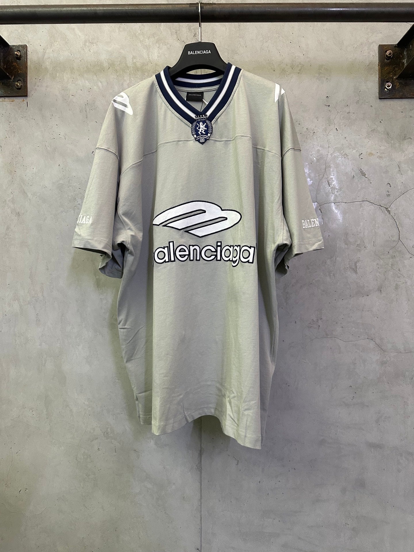 Light sage short-sleeve T-shirt with navy striped collar and crest patch at neckline