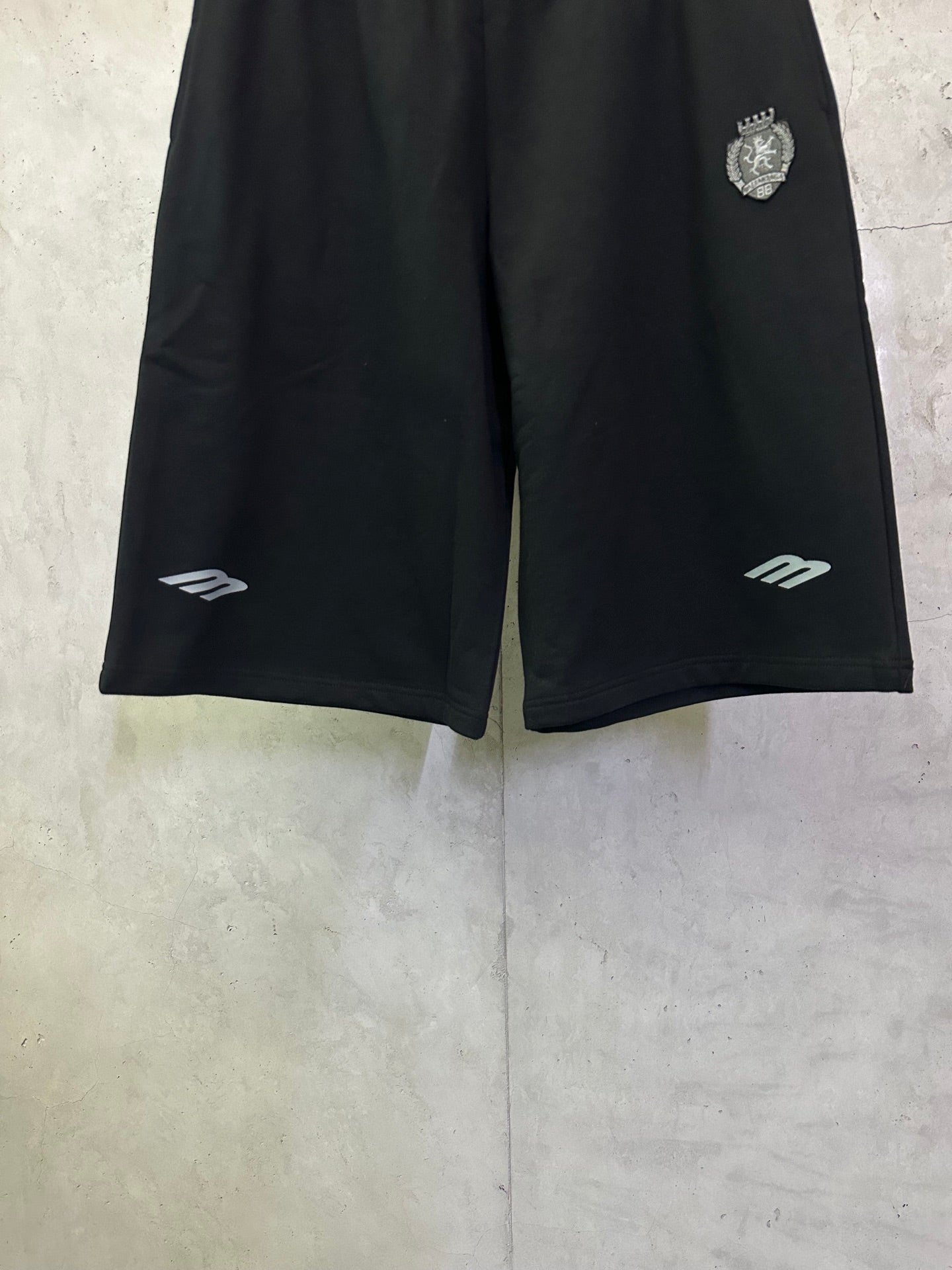Black shorts front view with elastic waist, small logo marks near hems, side pockets.