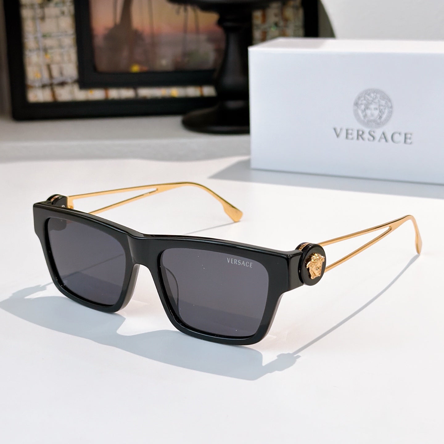 Black square sunglasses with dark lenses and gold-tone arms, Versace medallion details