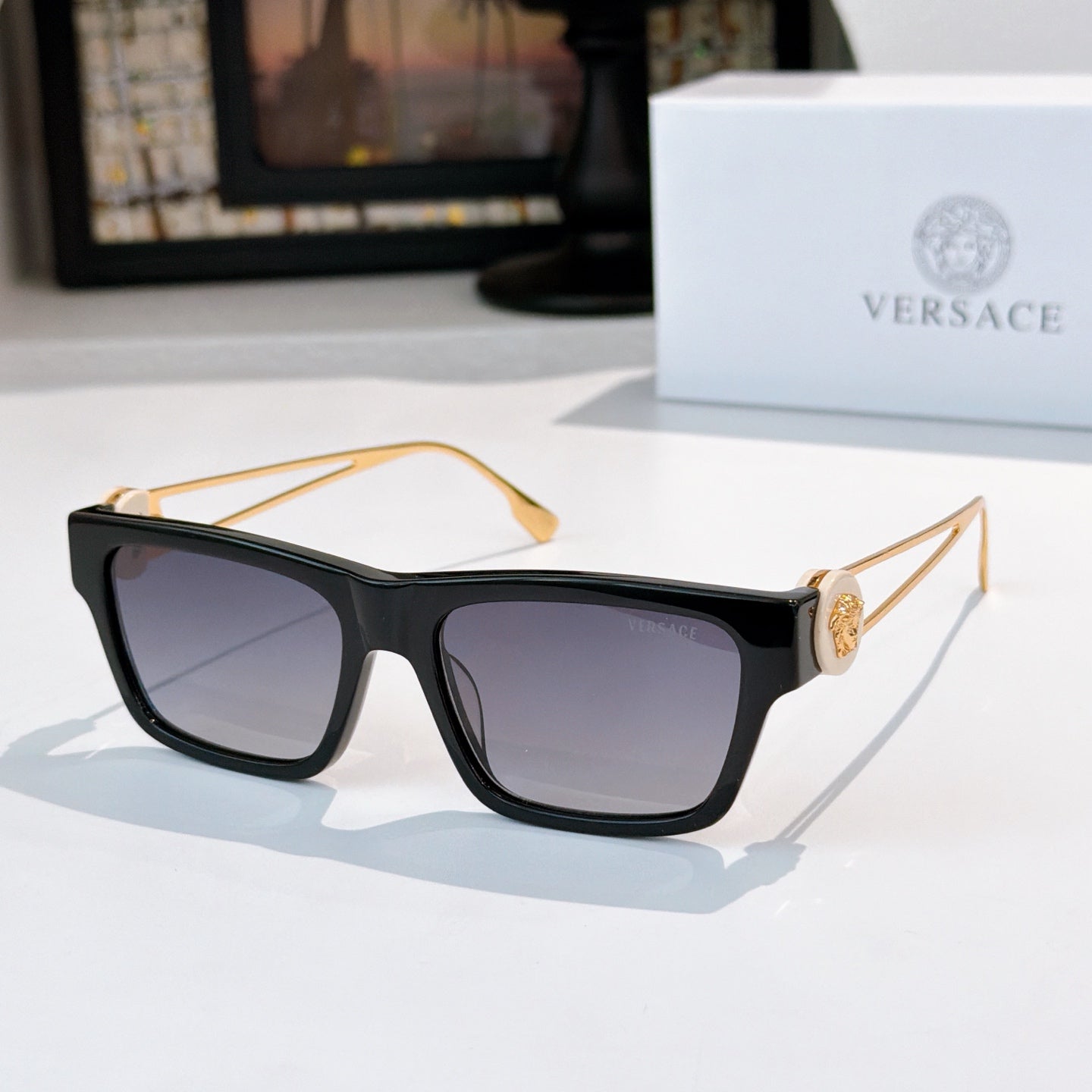 Black square sunglasses with dark lenses and gold-tone arms with emblem detail
