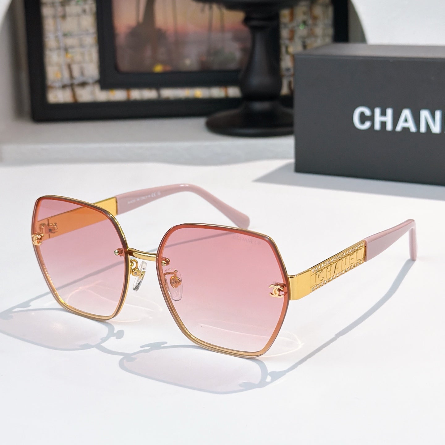 Sunglasses with rose-tinted lenses and gold-tone square frames, thin gold temple arms.