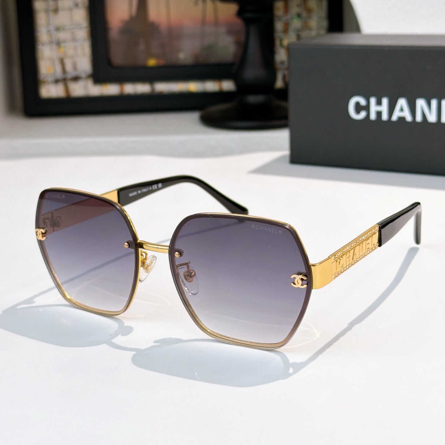 Sunglasses with blue-violet lenses, gold-tone square frames, black temples and gold logo bar.