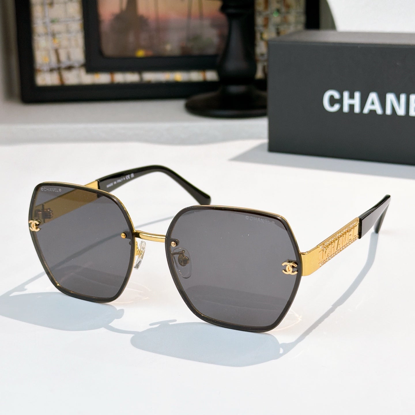 Sunglasses with dark gray lenses, gold-tone square frames, black temples and gold logo bar.