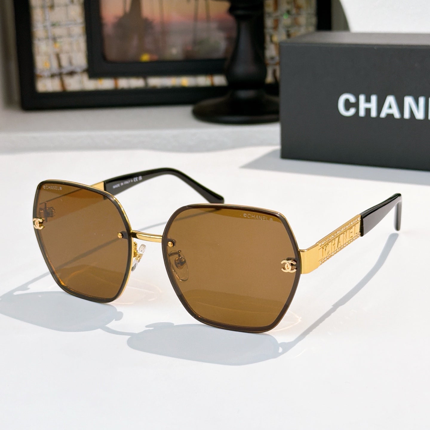 Sunglasses with brown lenses, gold-tone square frames, black temples and gold logo bar.