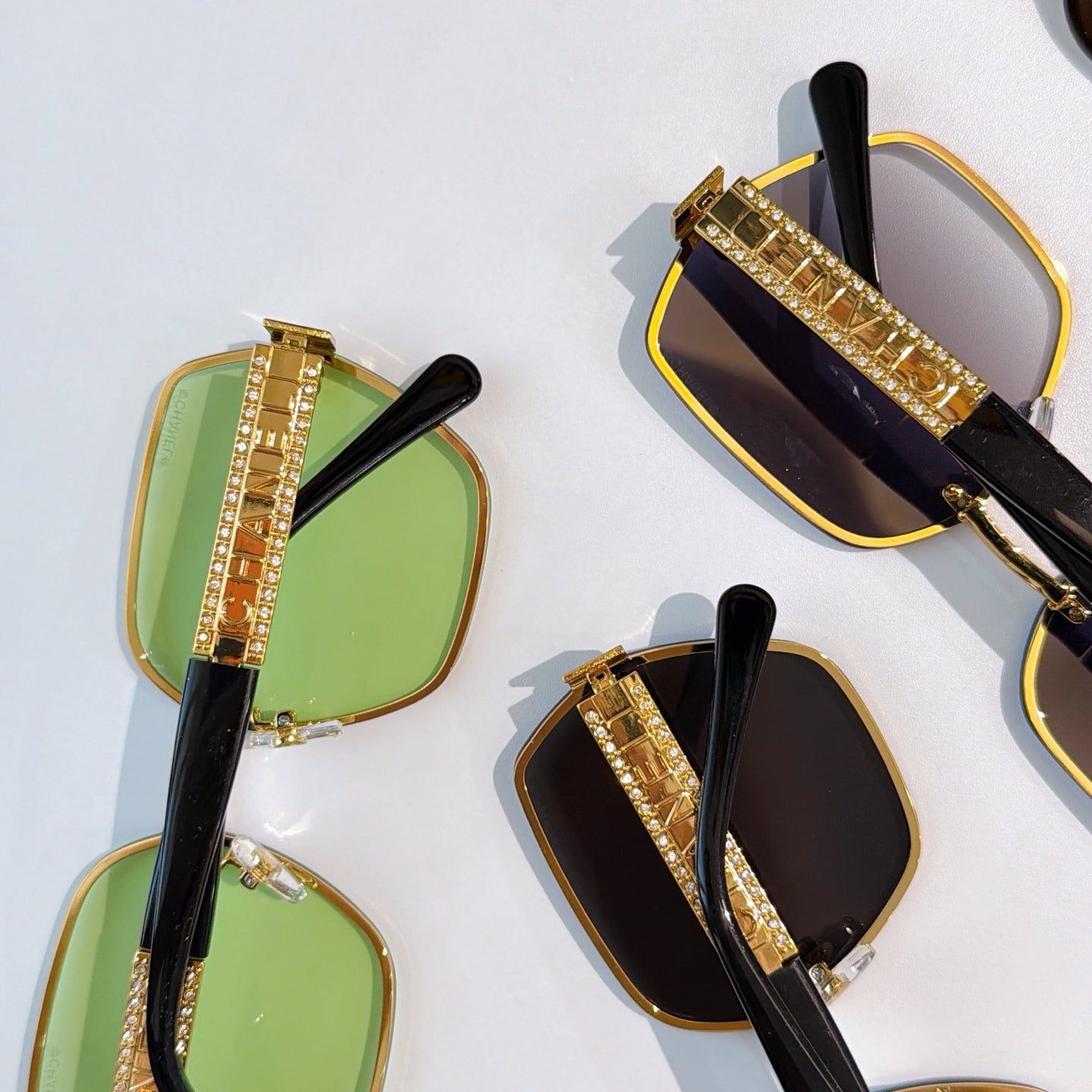 Sunglasses close-up set: green and black tinted square lenses with gold studded temple bars.