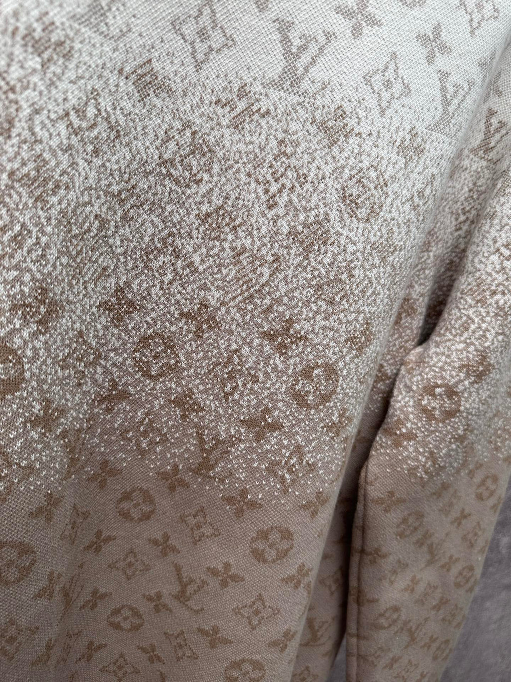 Close-up of light beige sweatshirt fabric with monogram pattern and speckled detail