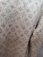 Close-up of light beige sweatshirt fabric with monogram pattern and speckled detail