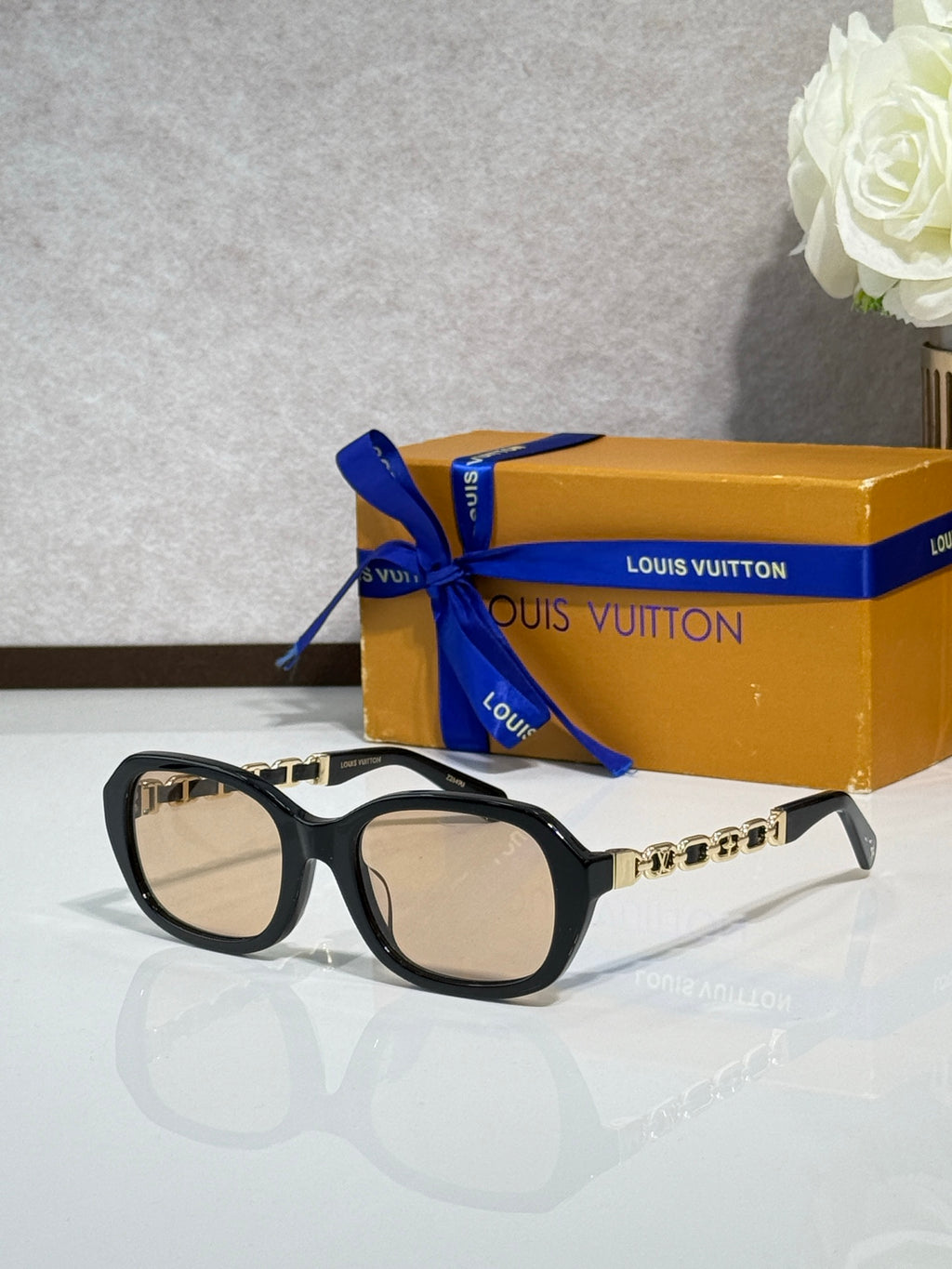 Sunglasses with black frame and tinted lenses, gold chain detail on arms