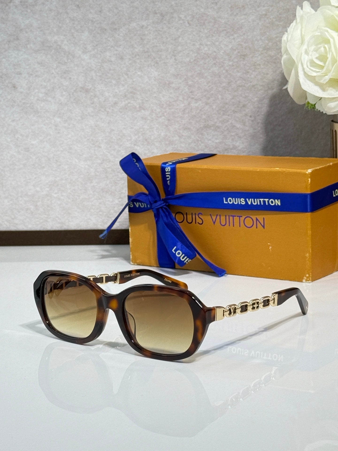 Sunglasses with tortoise-style frame and tinted lenses, gold chain detail on arms