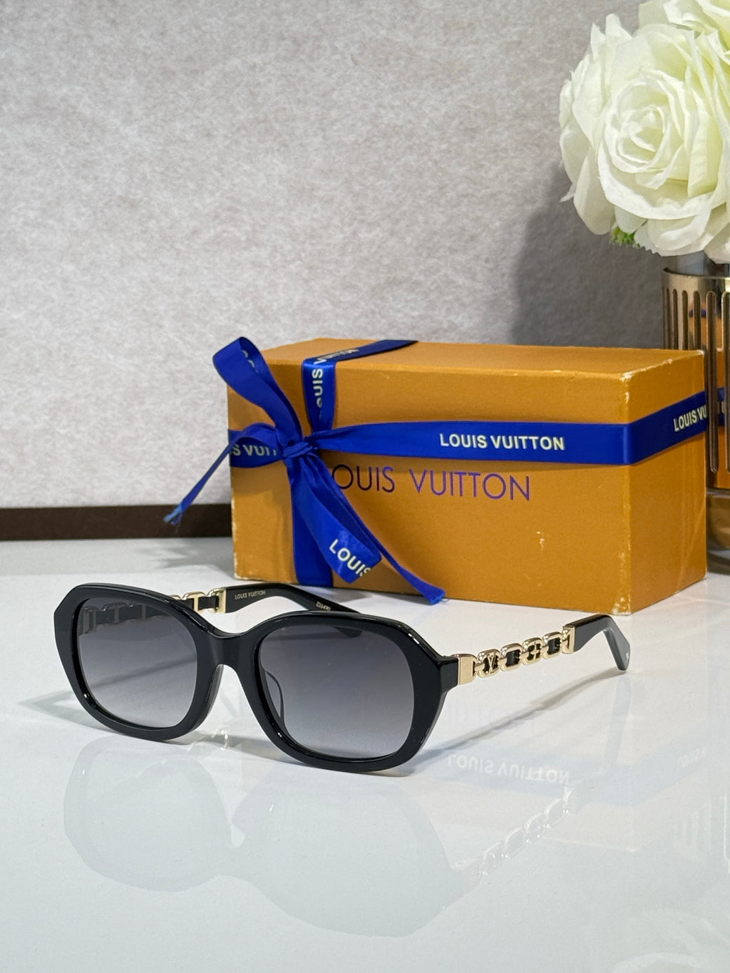 Louis Vuitton sunglasses with black frame and dark lenses, gold chain detail on arms