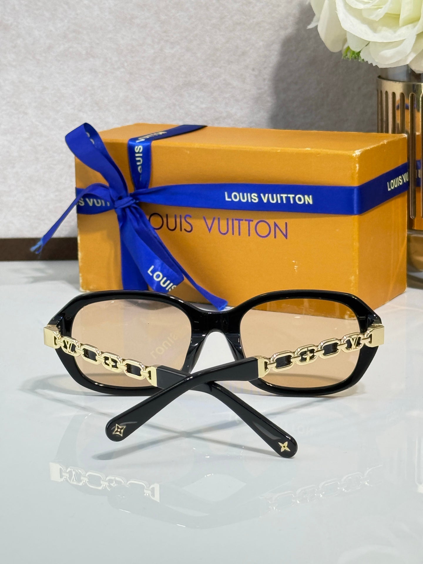 Sunglasses with black frame and light-tinted lenses, gold chain with charm accents