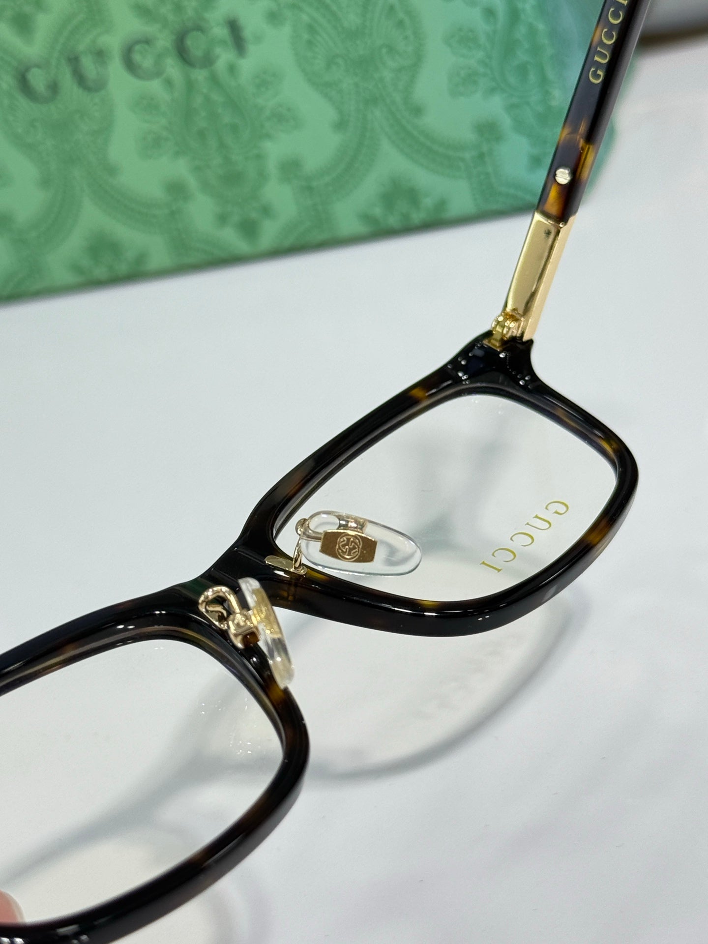 Close-up of black eyeglass frame with clear lens and gold-tone bridge hardware