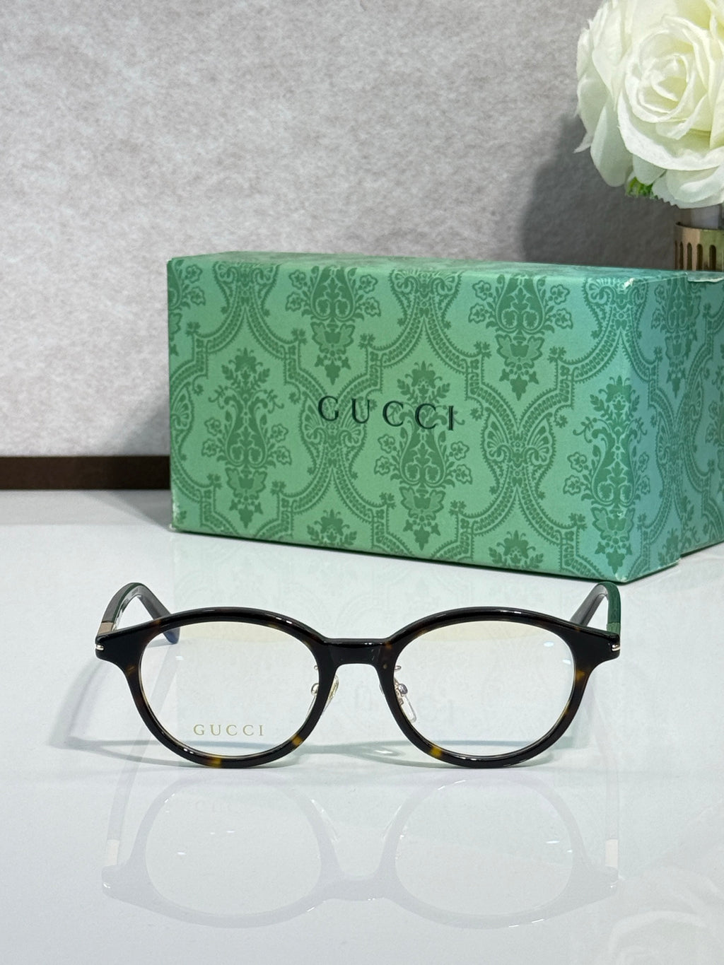 Black round eyeglasses with clear lenses and gold logo temples, front angle.