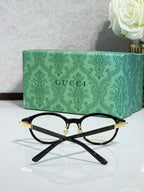 Black eyeglasses with gold-accent temples and clear lenses, crossed view.
