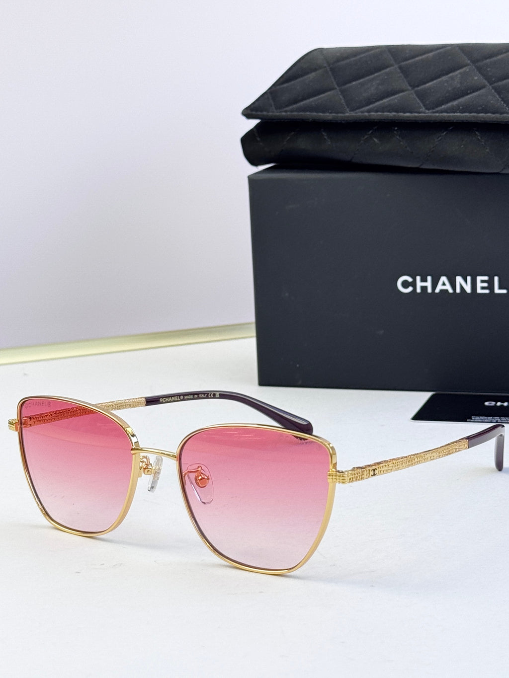 Chanel sunglasses with pink tinted lenses, gold-tone metal frames, rounded cat-eye shape