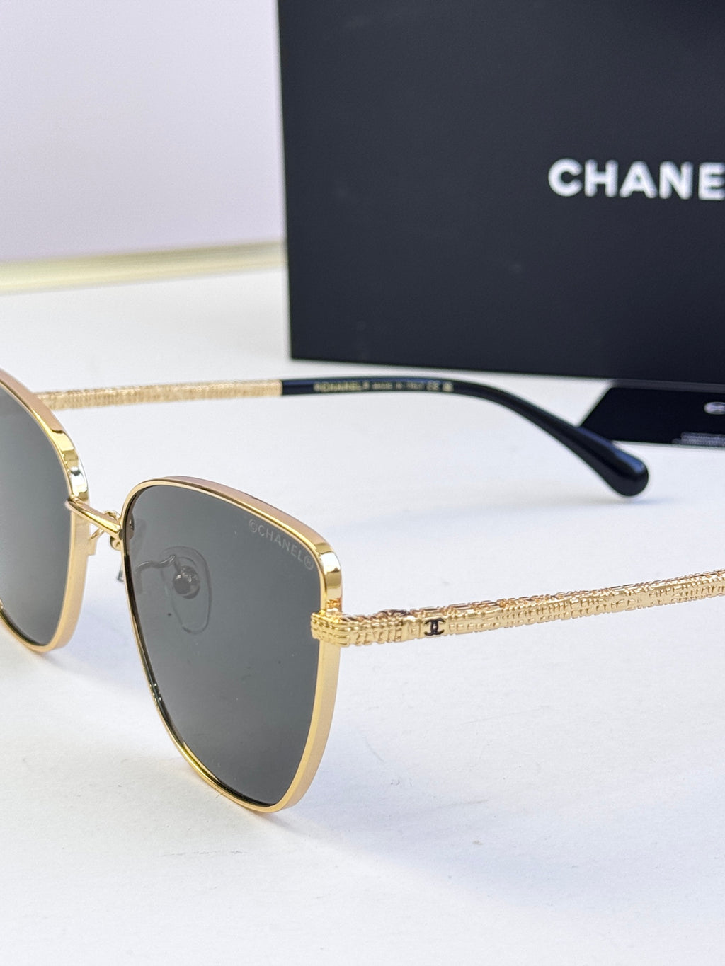 Chanel sunglasses close-up, gold-tone metal frame, dark lenses, black temple tip