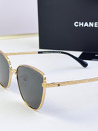 Chanel sunglasses close-up, gold-tone metal frame, dark lenses, black temple tip