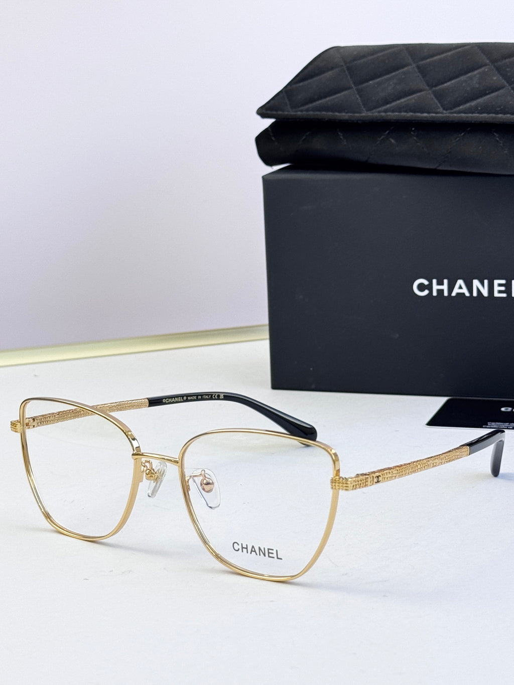 Gold metal eyeglasses with clear lenses, square frames, and engraved temples