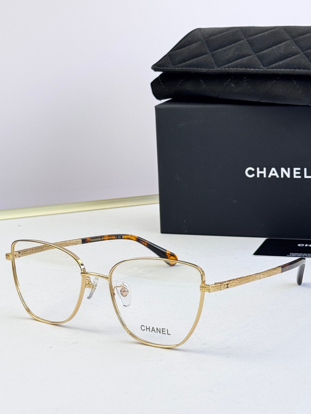 Gold eyeglasses with clear lenses; tortoise-pattern bridge and textured temples