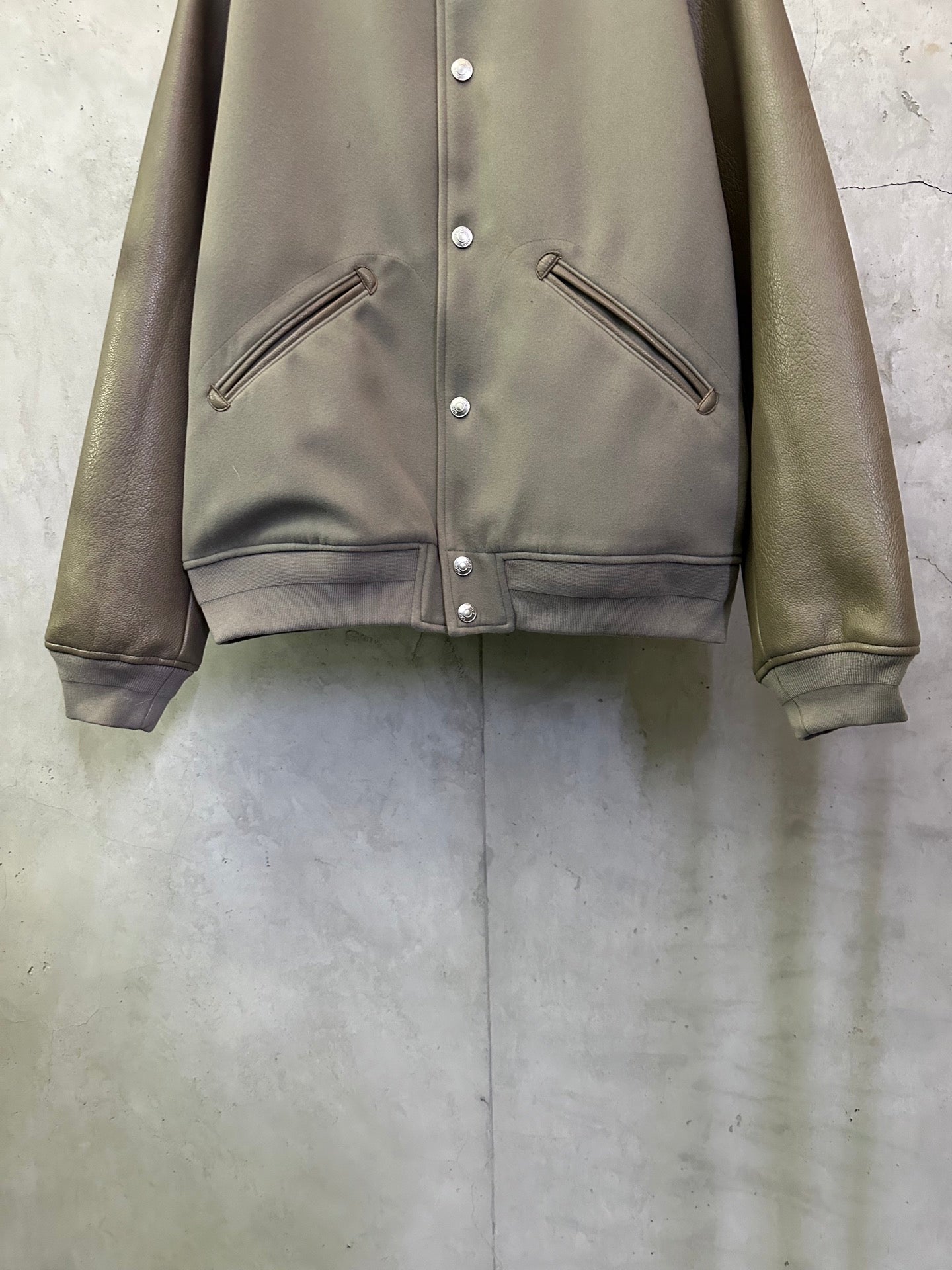 Olive jacket front with snap buttons and diagonal zip pockets