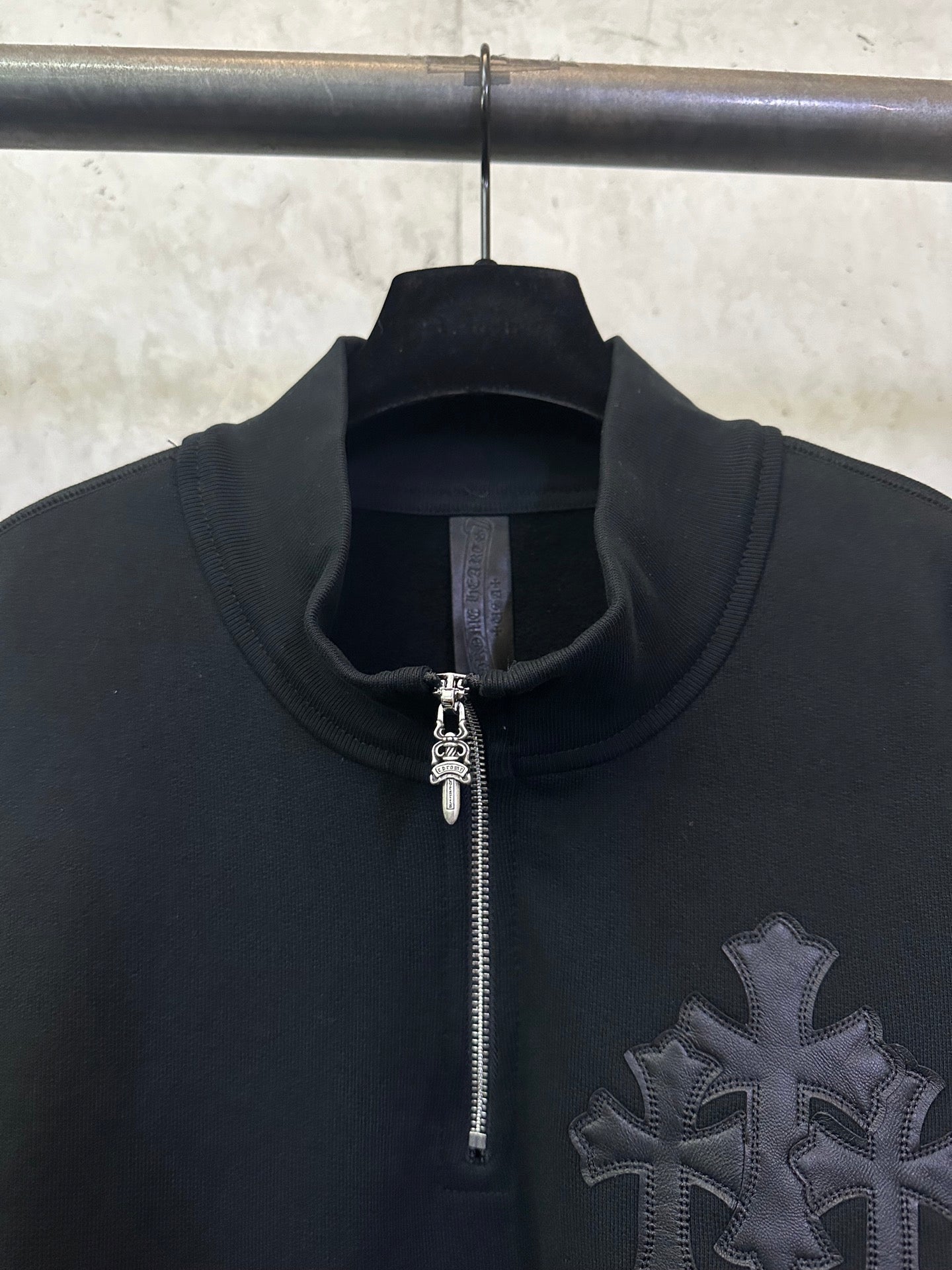 Black hoodie with half-zip, zipper pull, and raised cross emblem detail.