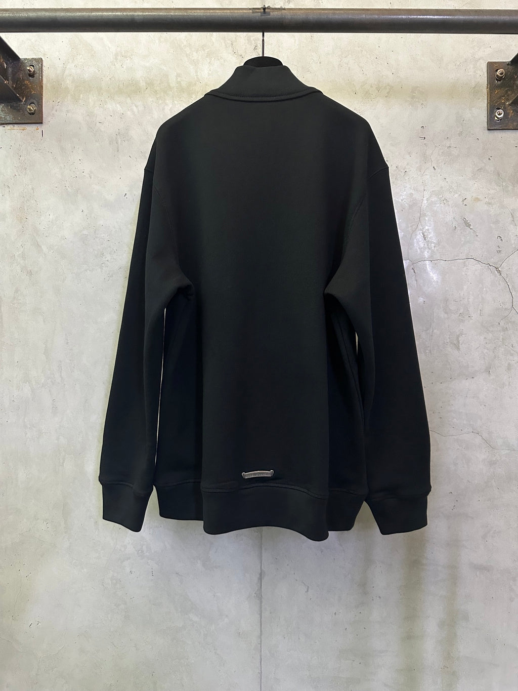 Black long-sleeve hoodie, back view, with small logo near hem.