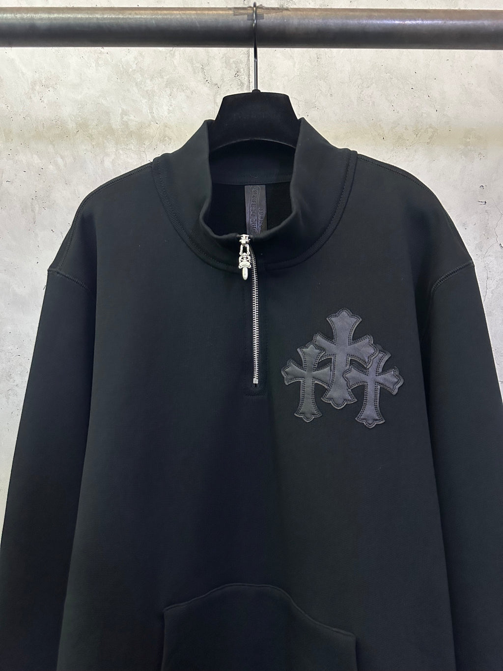 Black long-sleeve hoodie with half-zip and silver-toned cross emblem on chest.