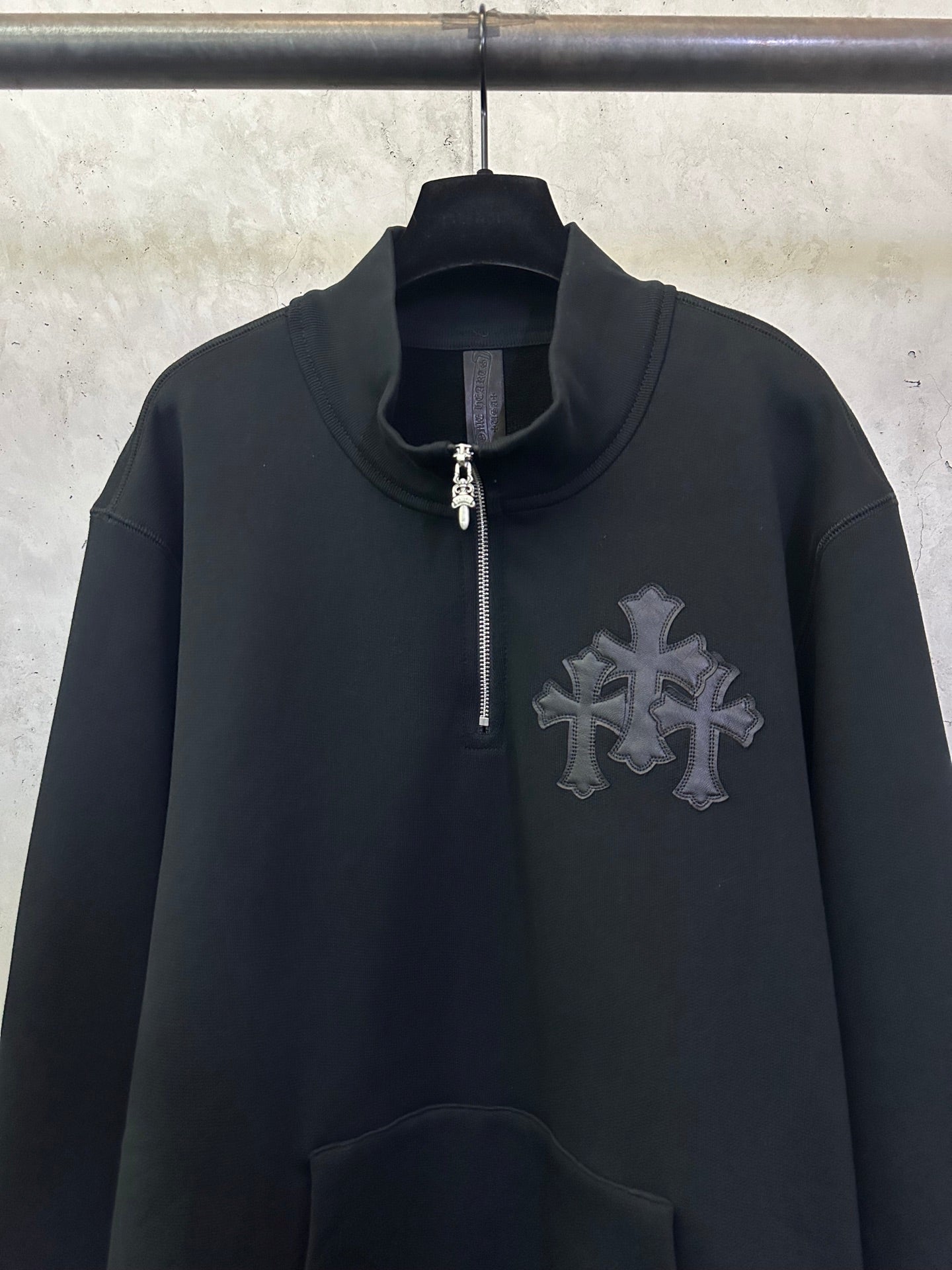 Black long-sleeve hoodie with half-zip and silver-toned cross emblem on chest.