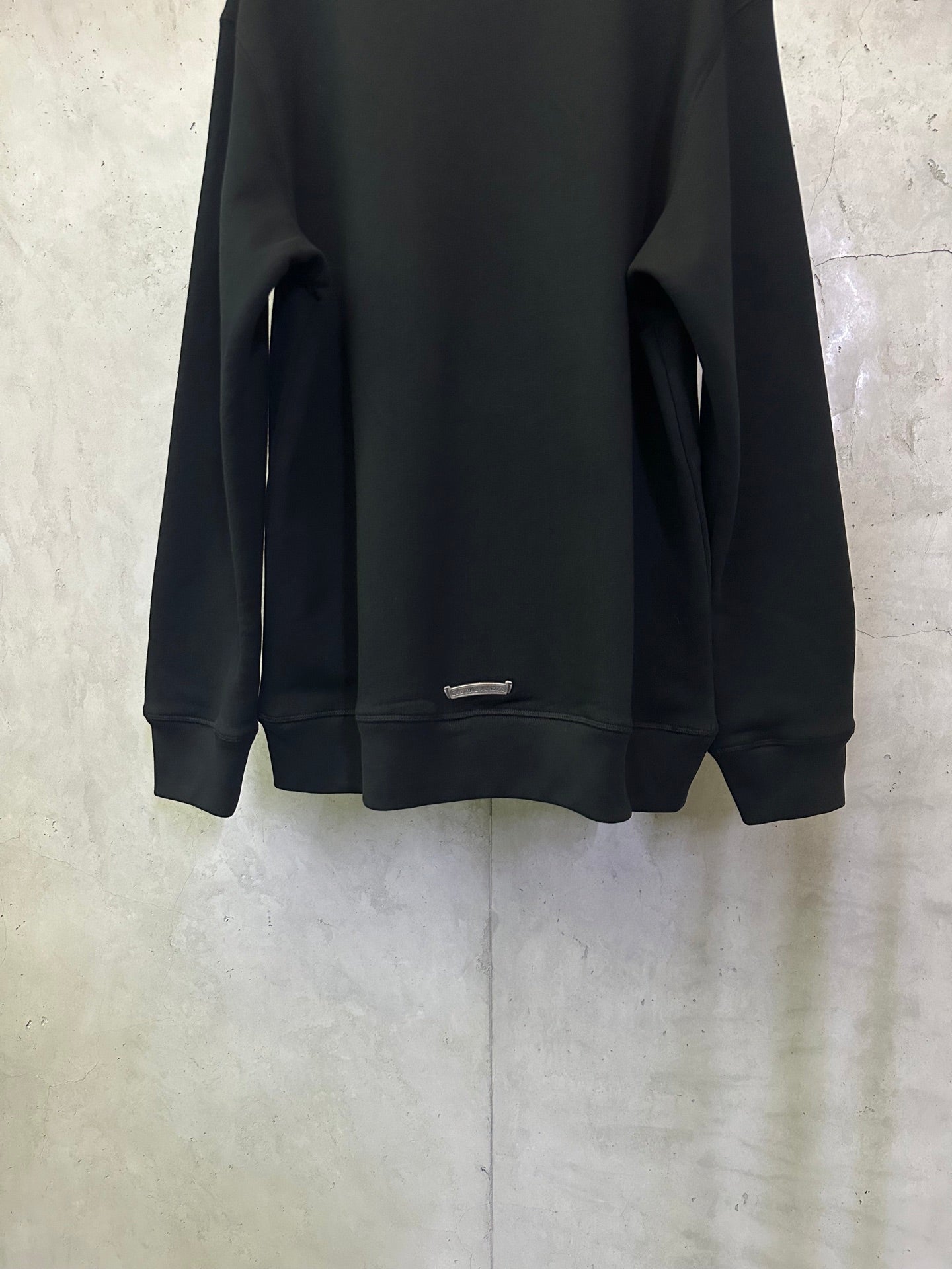 Black long-sleeve hoodie back with small metal bar near hem.