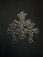 Embroidered cross patch in gray thread on black hoodie fabric.