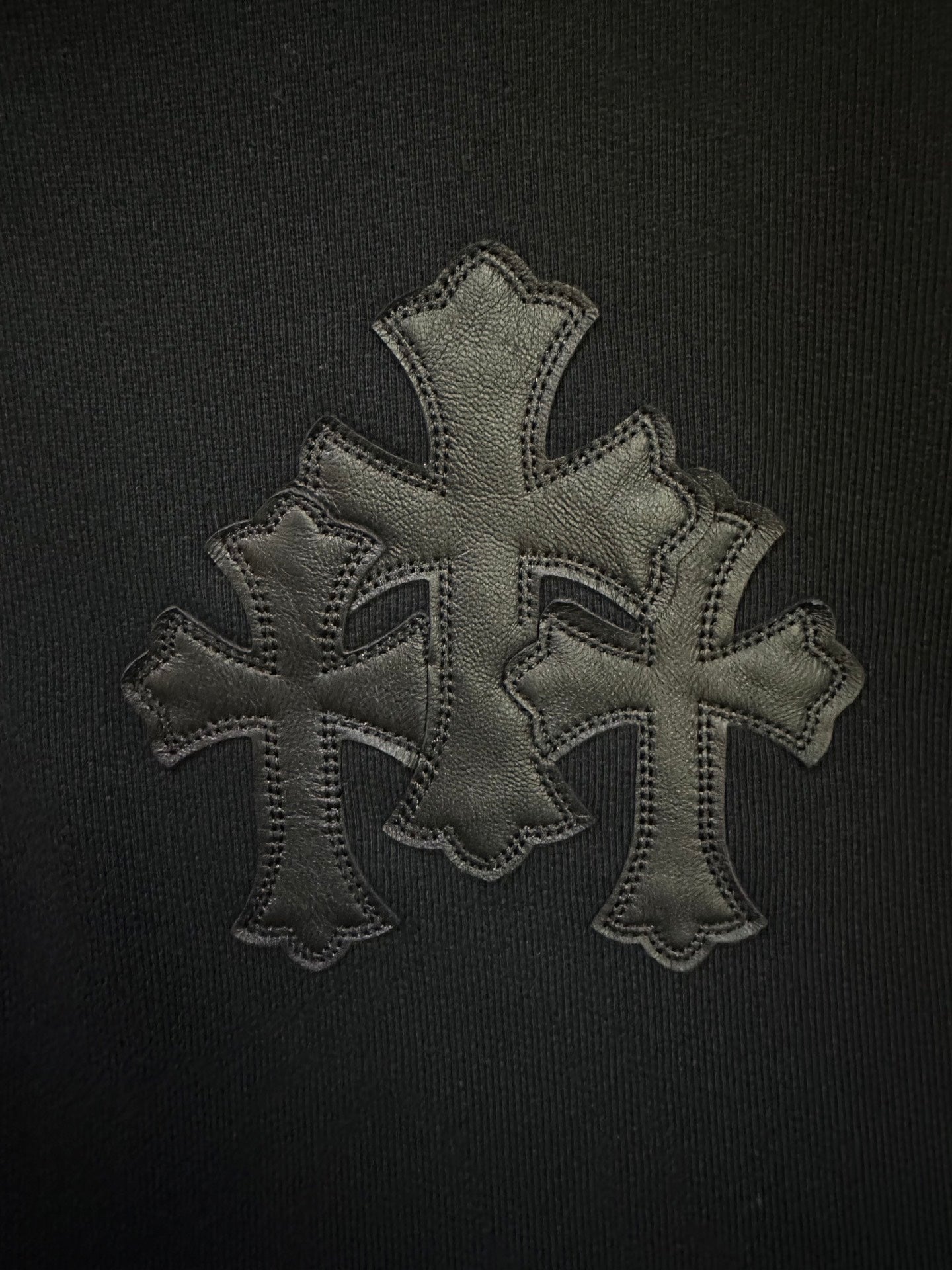 Embroidered cross patch in gray thread on black hoodie fabric.