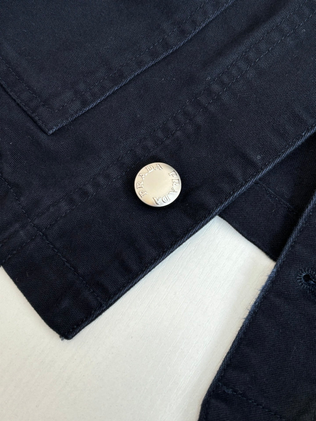 Prada long jacket sleeve close-up with round metal button on dark navy fabric