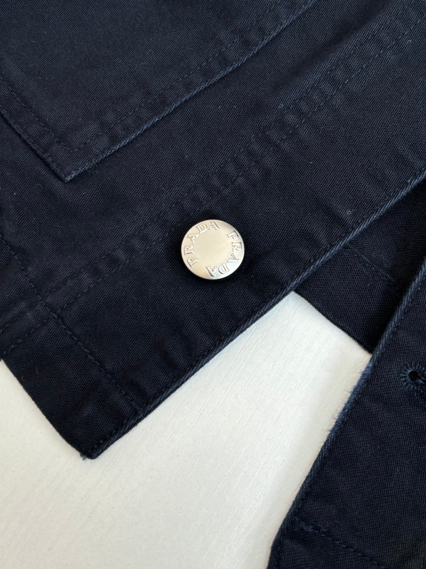 Prada long jacket sleeve close-up with round metal button on dark navy fabric