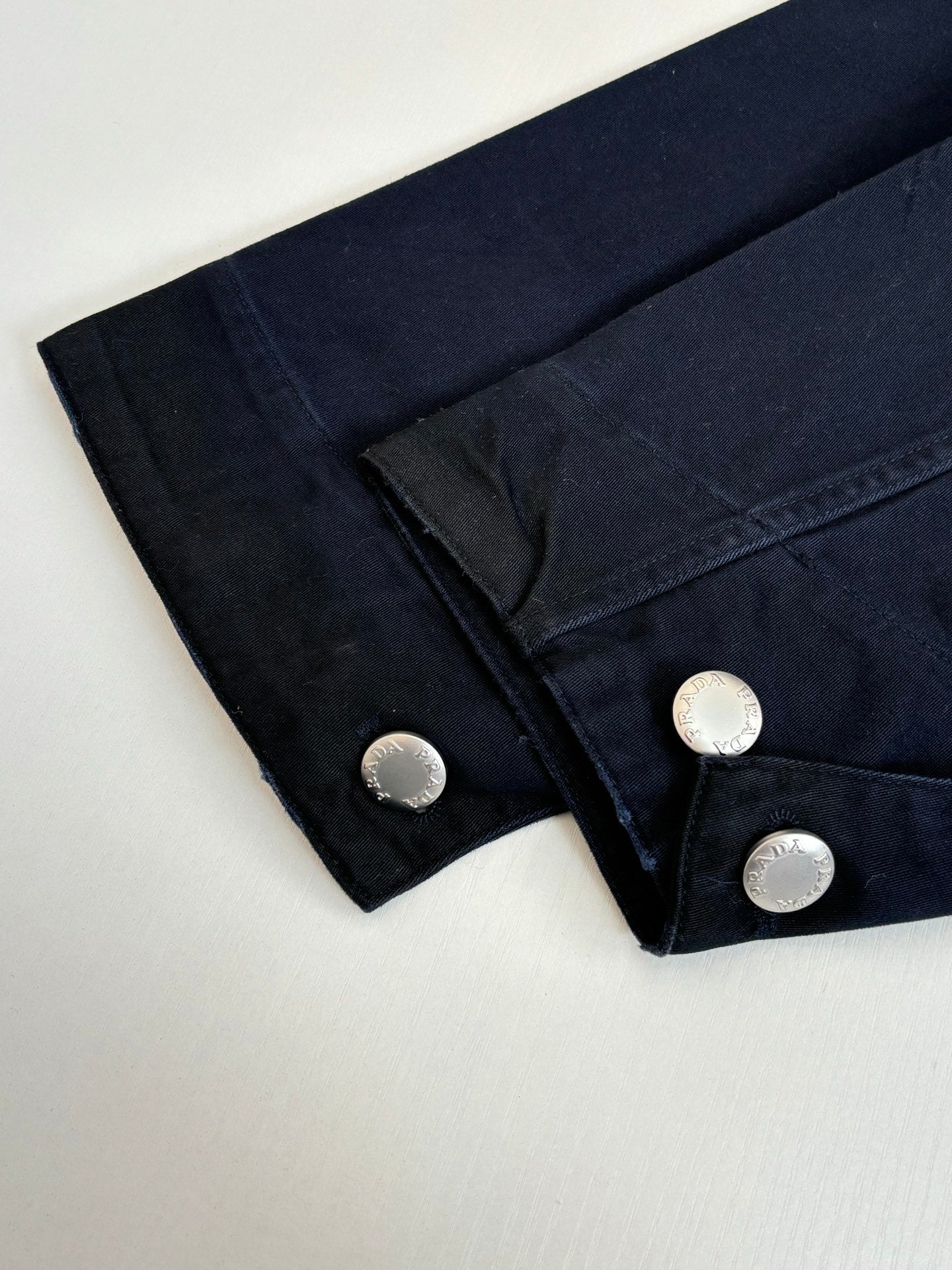 Prada long jacket cuff close-up with round metal buttons on dark navy