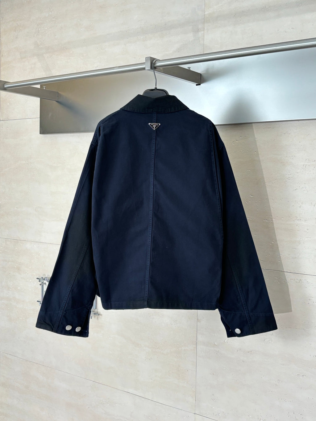 Navy long jacket with pointed collar and snap buttons, back view on hanger