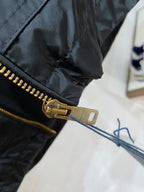 Gold front zipper and pull on black hooded jacket sleeve, close-up detail.