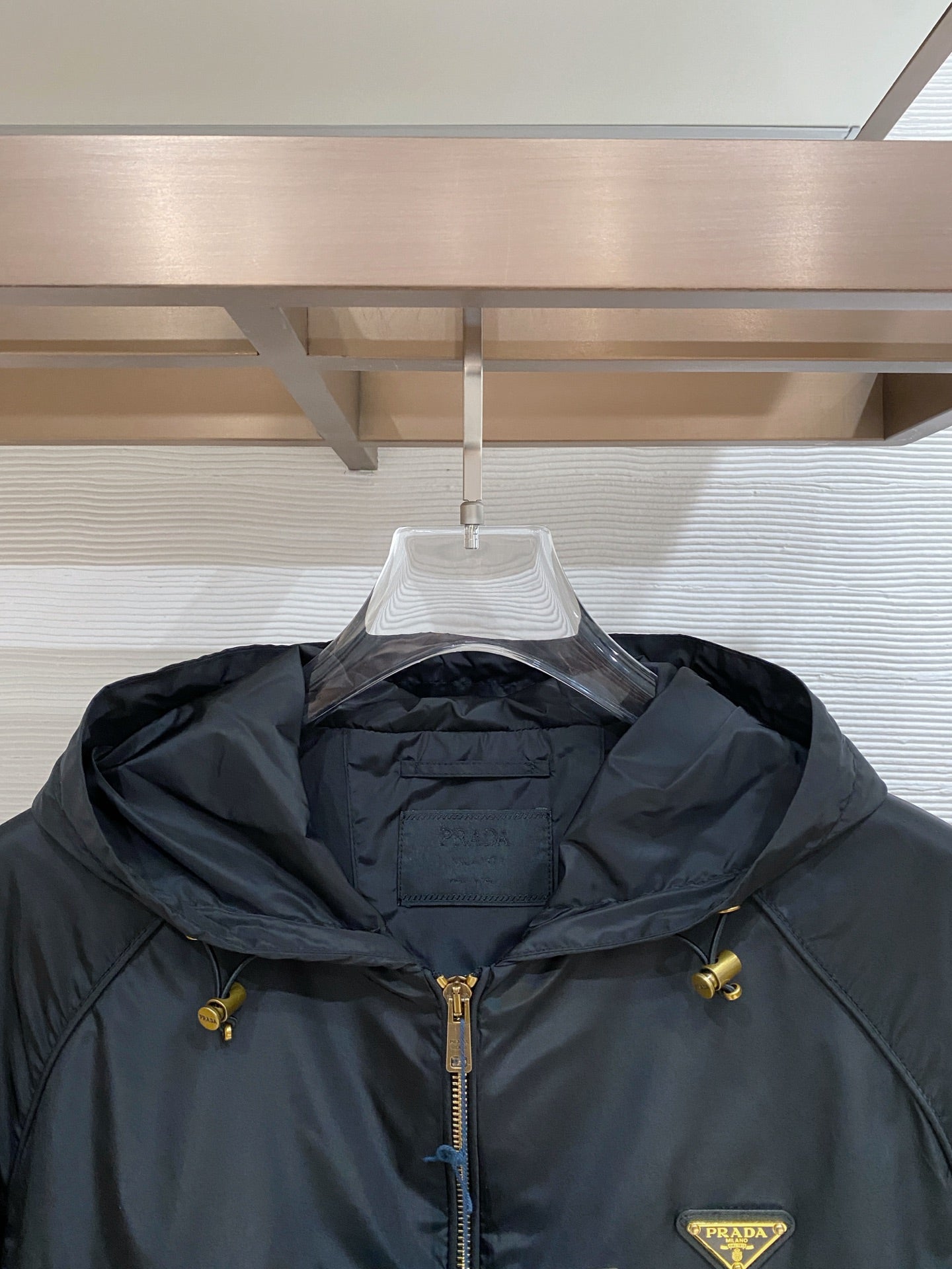 Black hooded jacket neckline detail with front zip, drawcords, and Prada logo patch.