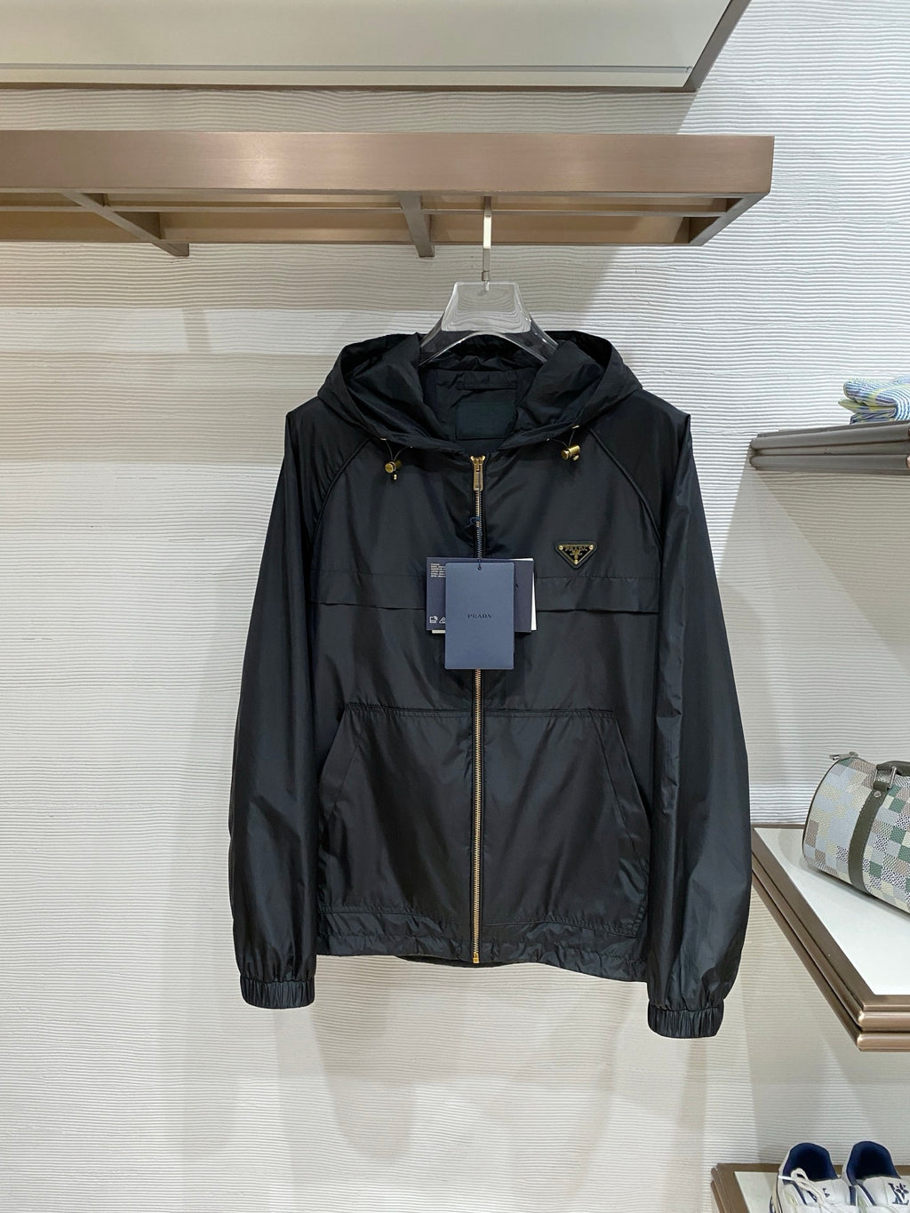 Black hooded jacket with front zip, gold hardware, and small Prada logo patch