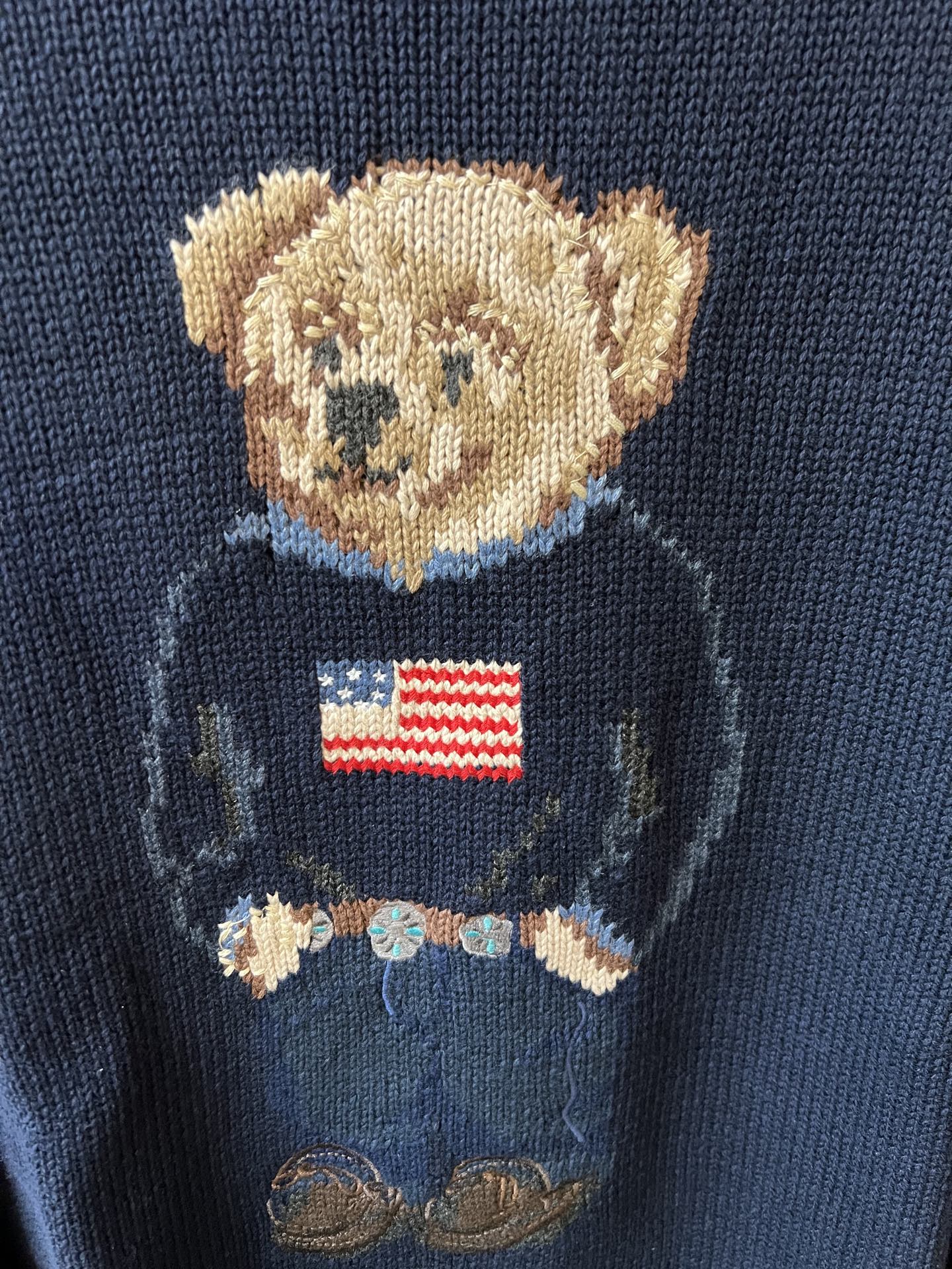 Close-up navy knit sweater showing teddy bear face and American flag